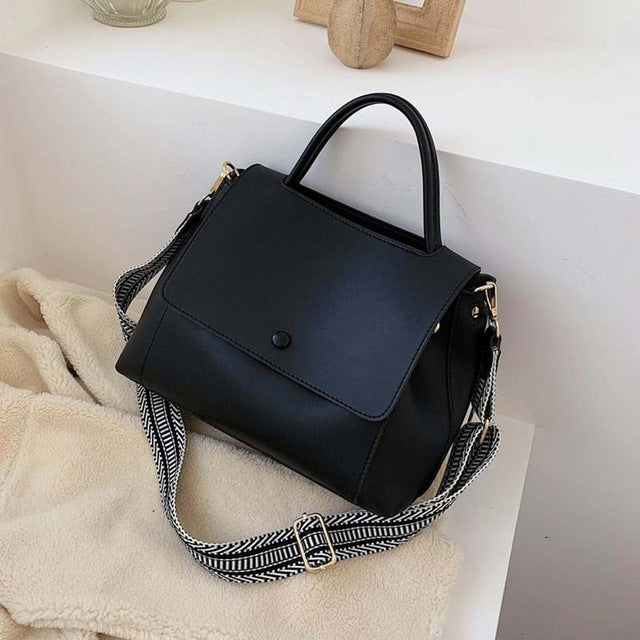 Black handbag with a patterned strap on a white surface
