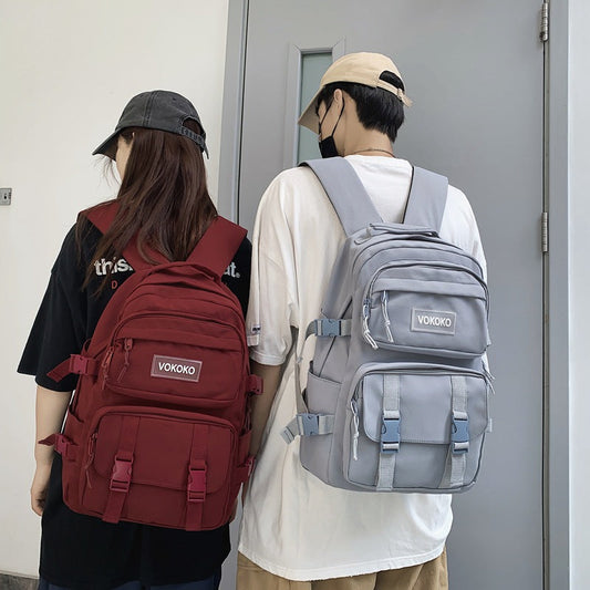 Two people wearing VOKOKO backpacks, one red and one gray, standing against a plain background.