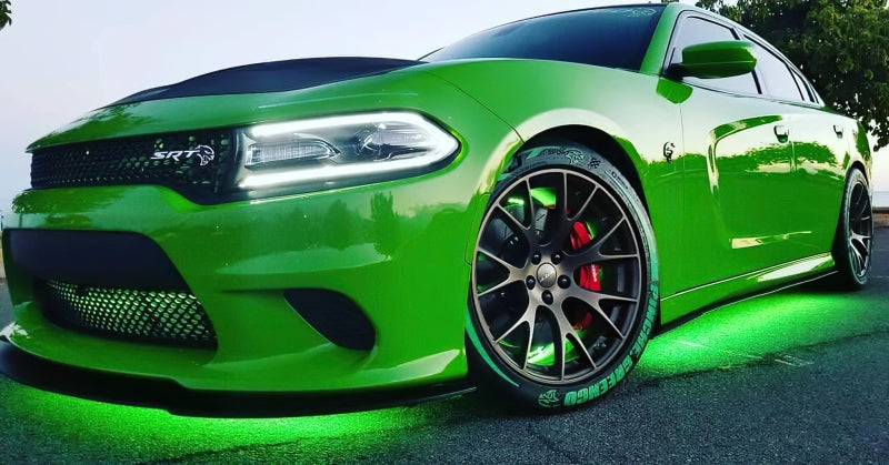 Green sports car with black roof and red brake calipers on a road with underbody lighting.