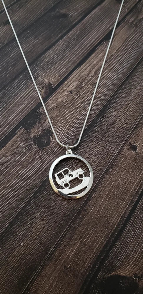 Silver necklace with a circular pendant featuring an off-road vehicle design on a wooden surface.