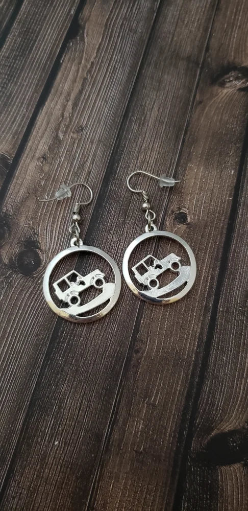 Silver earrings with jeep cutout design on a wooden surface