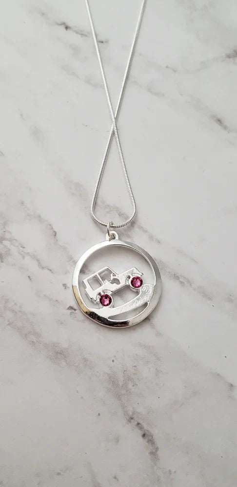 Silver necklace with a round pendant featuring a car design and two red gemstones on a marble surface.