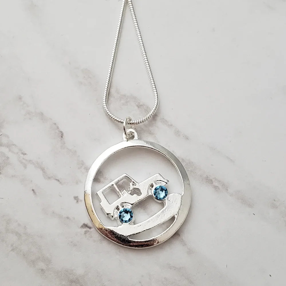 Silver necklace with a circular pendant featuring a Jeep design and blue stones on a marble surface.
