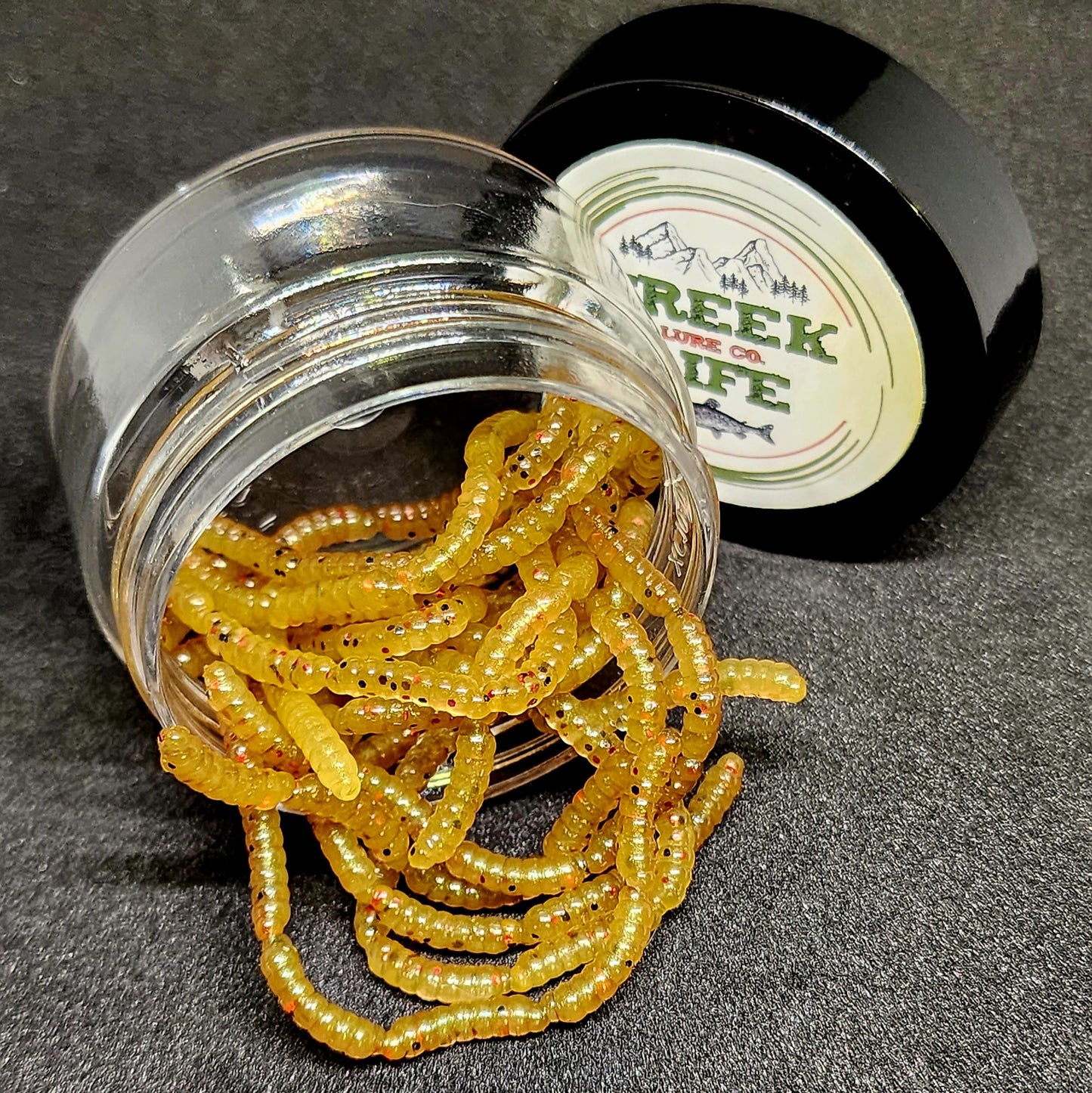 Jar of yellow fishing lures with a container labeled Creek life on a dark surface