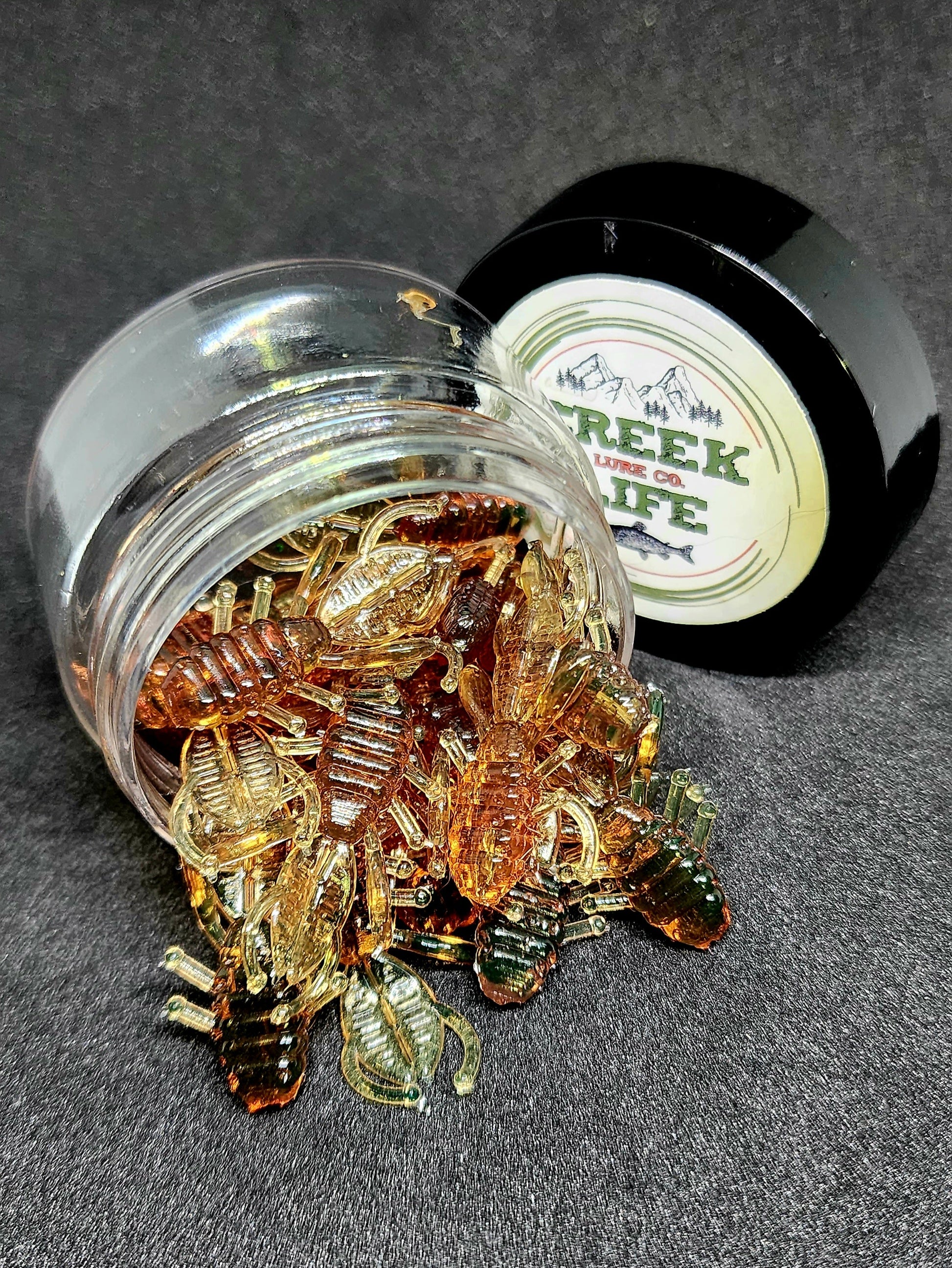 Glass jar filled with amber-colored fishing lures on a dark surface, with a container labeled 'Creek Life' in the background.
