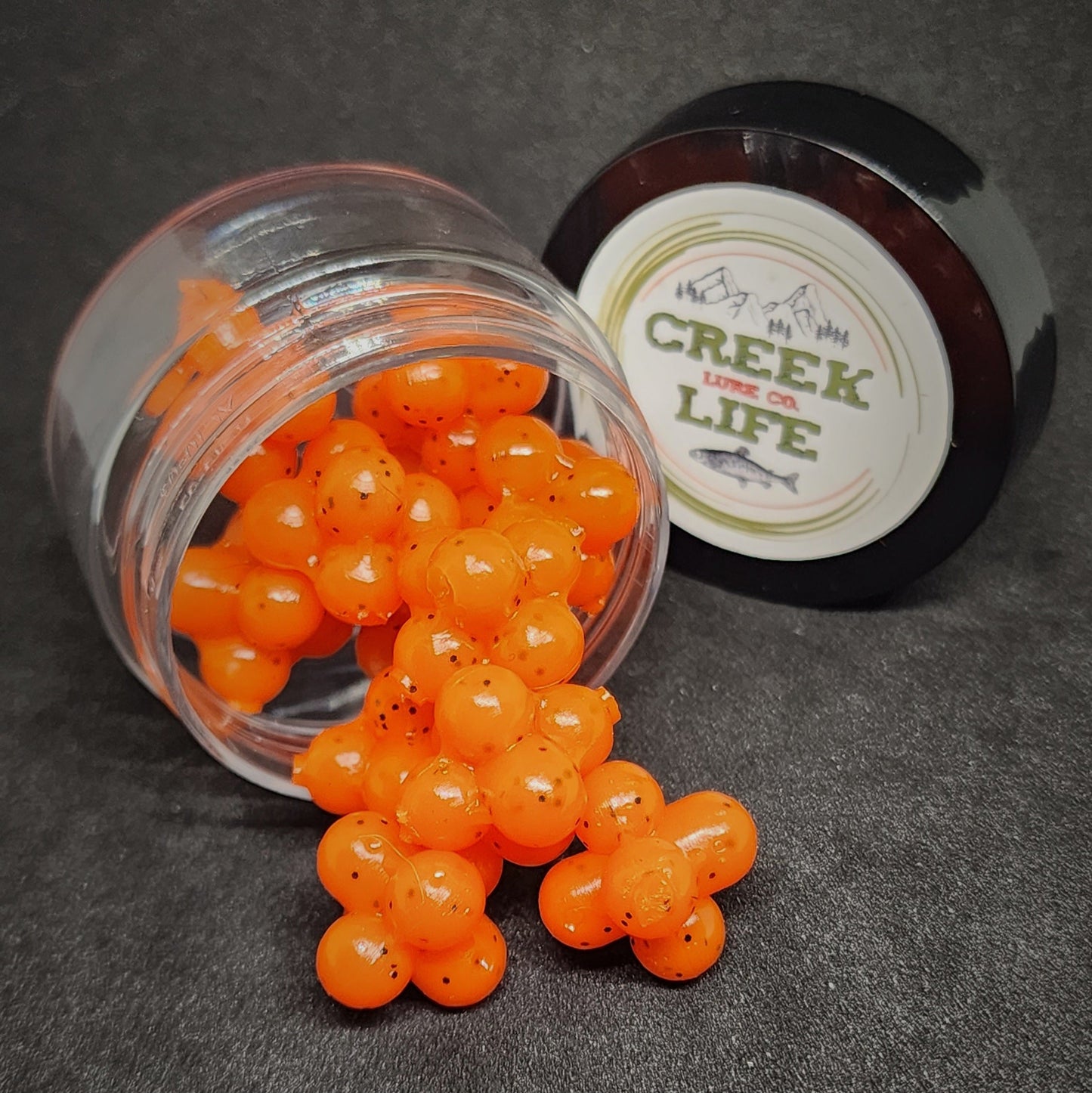 Orange fishing lures spilling out of a clear jar with a 'Creek Life' container in the background.