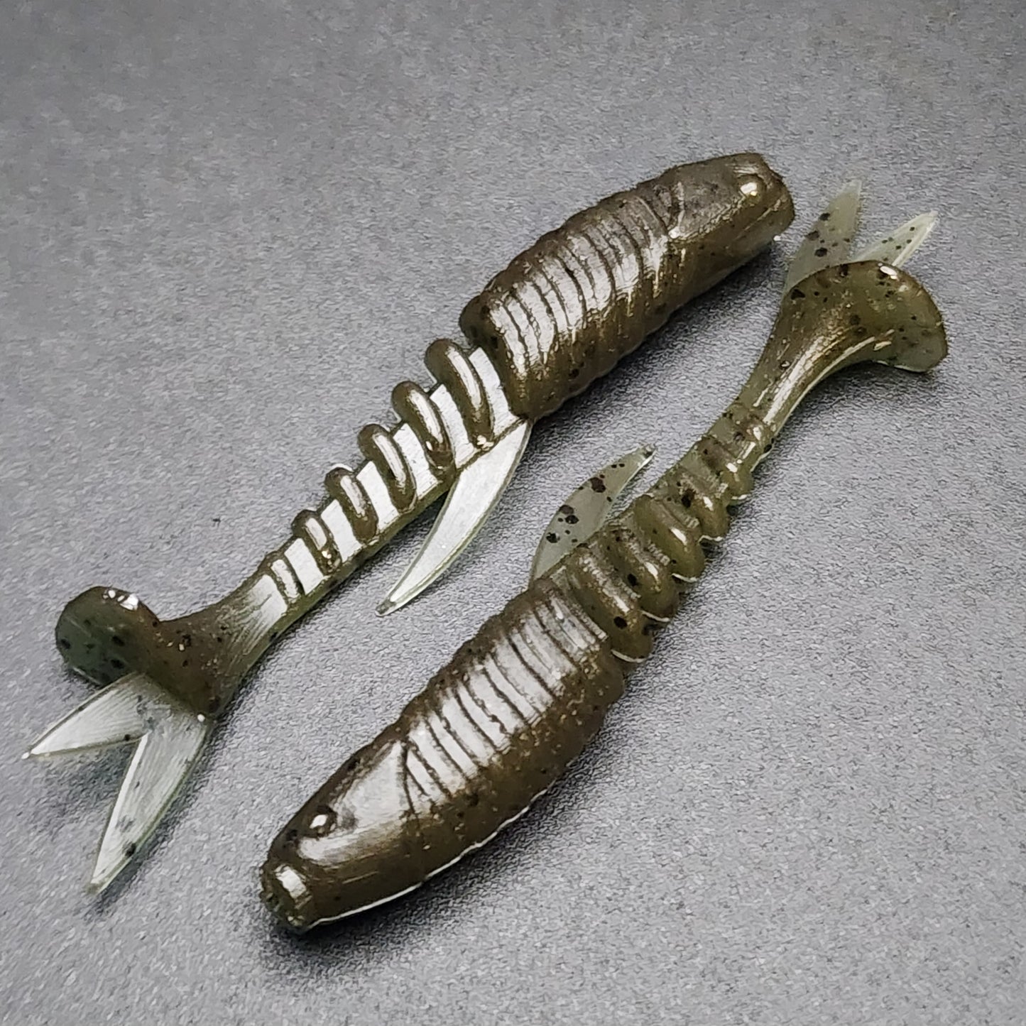 Two fishing lures resembling worms on a gray surface