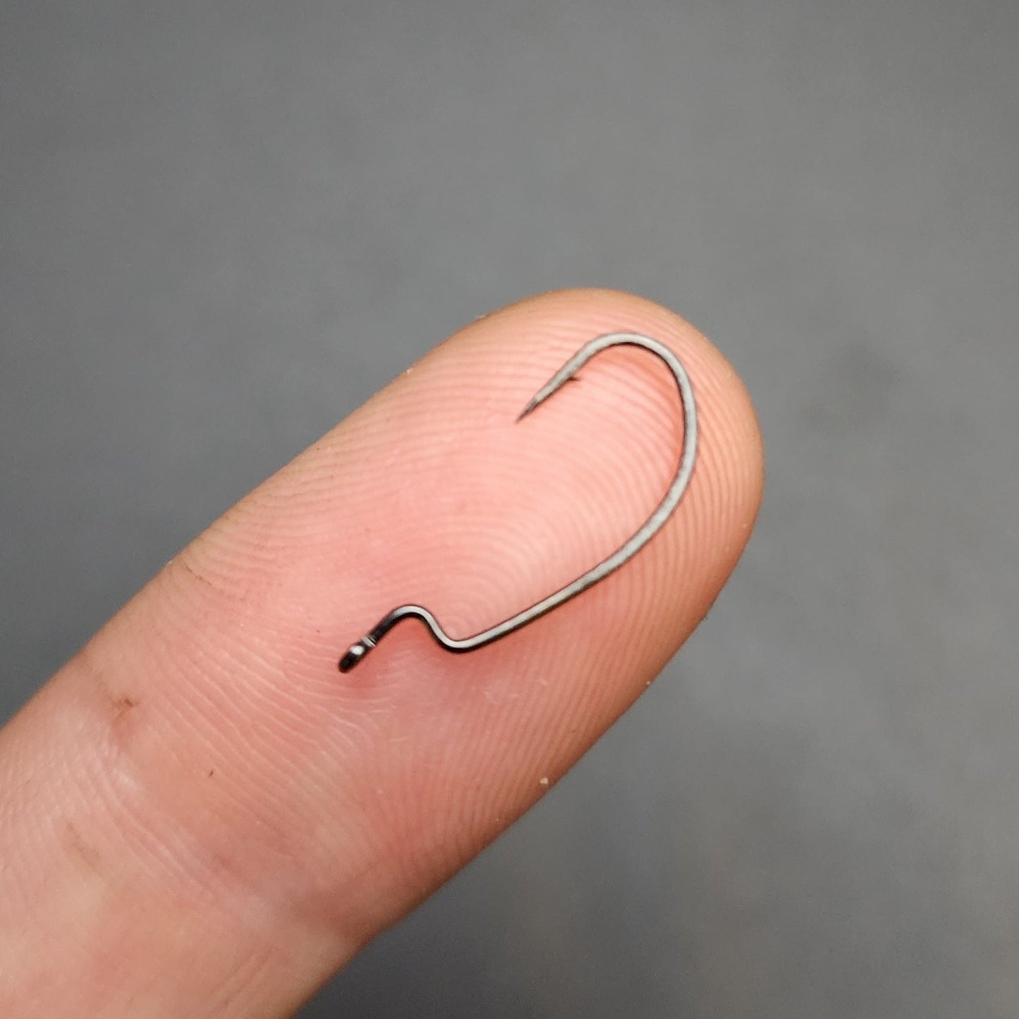 Small fishing hook held between fingers against a gray background