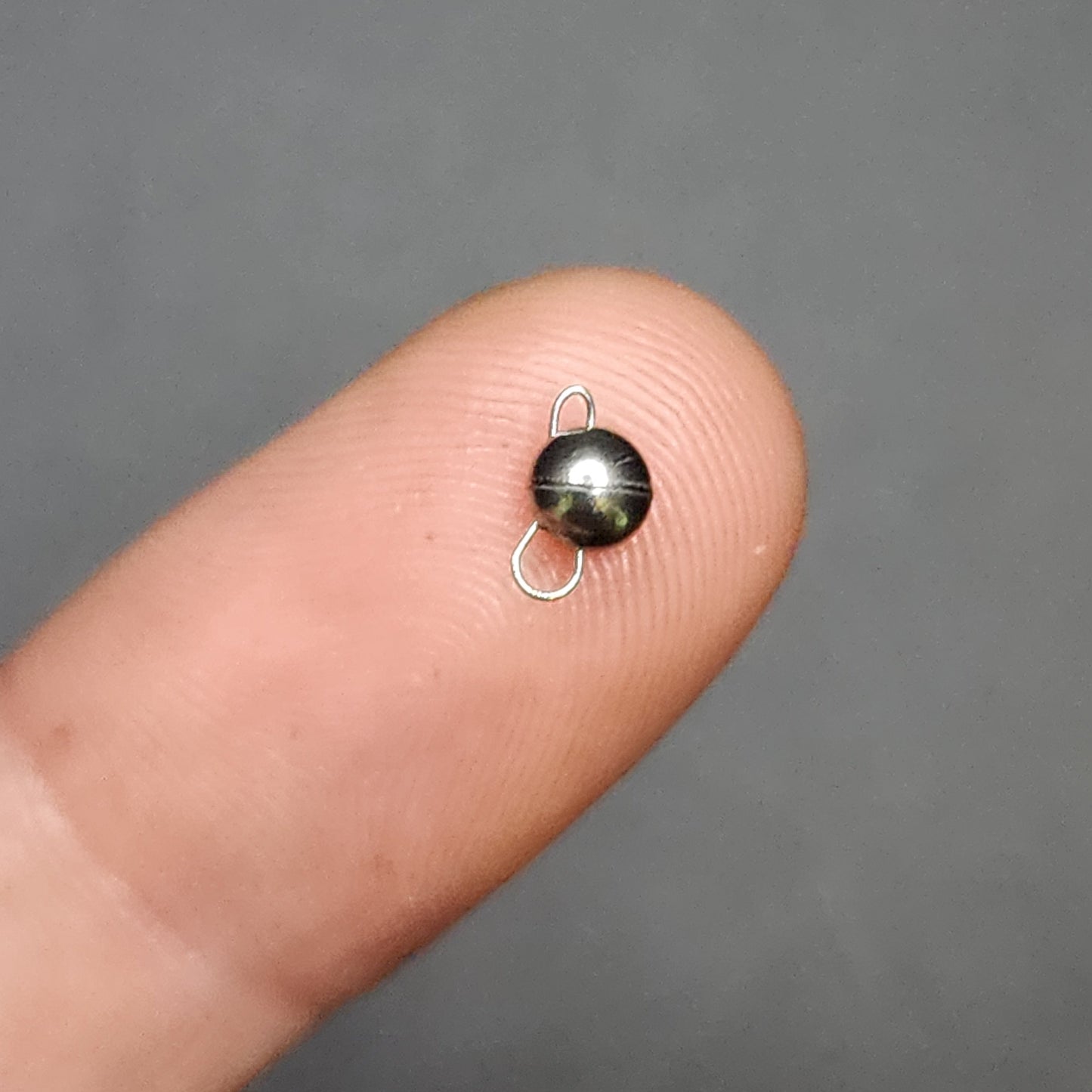 Small metallic sinker on a finger against a gray background