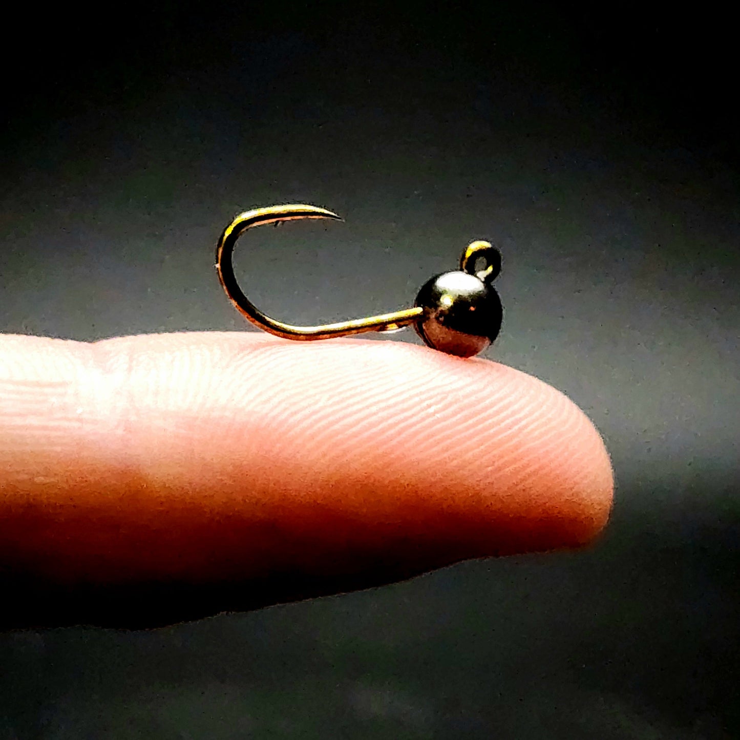 Gold fishing hook on a finger against a dark background