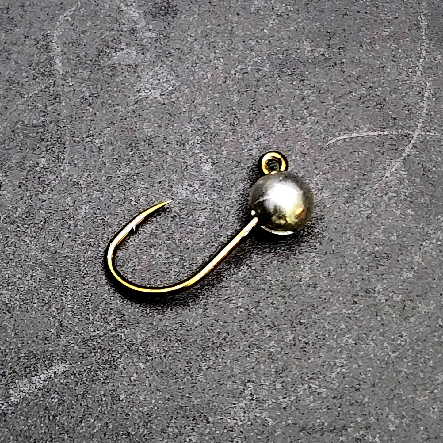 Fishing hook with a spherical weight on a gray surface