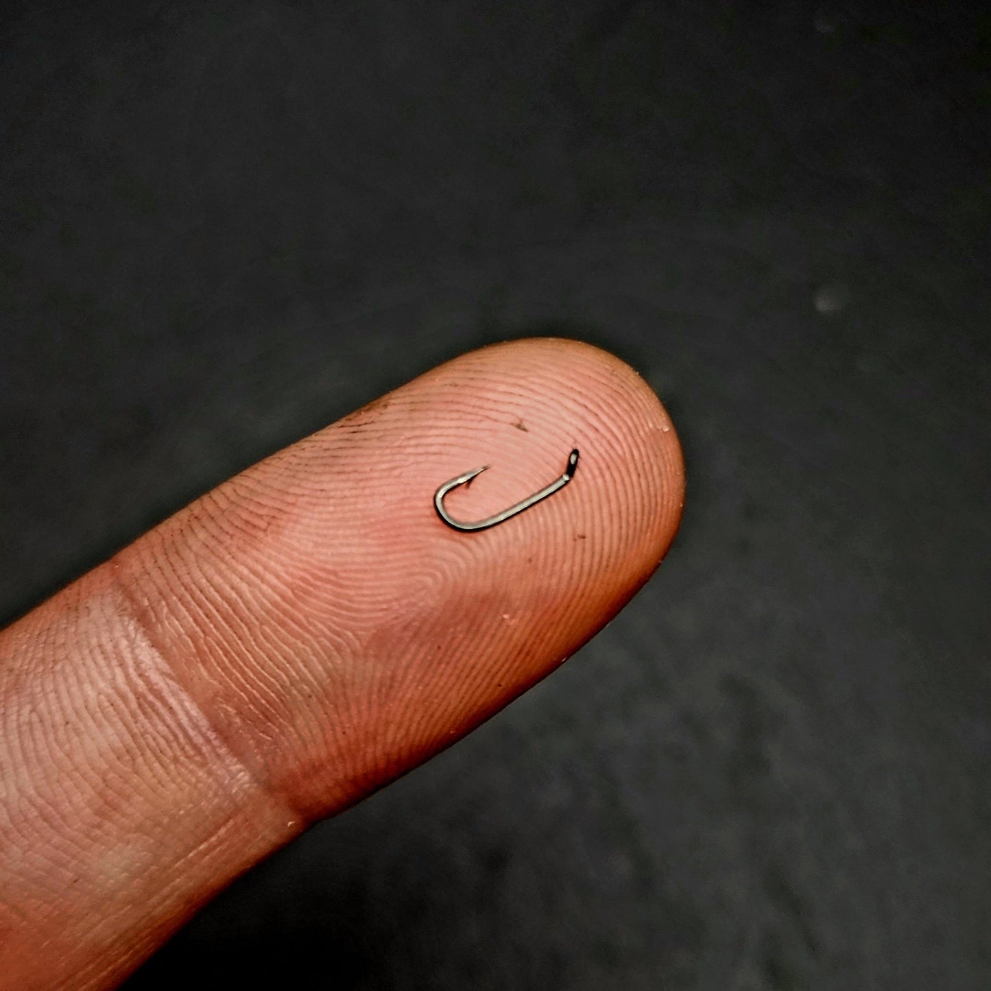 Fishing hook on a finger against a dark background