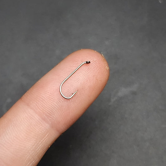 Small fishing hook on a finger against a dark background