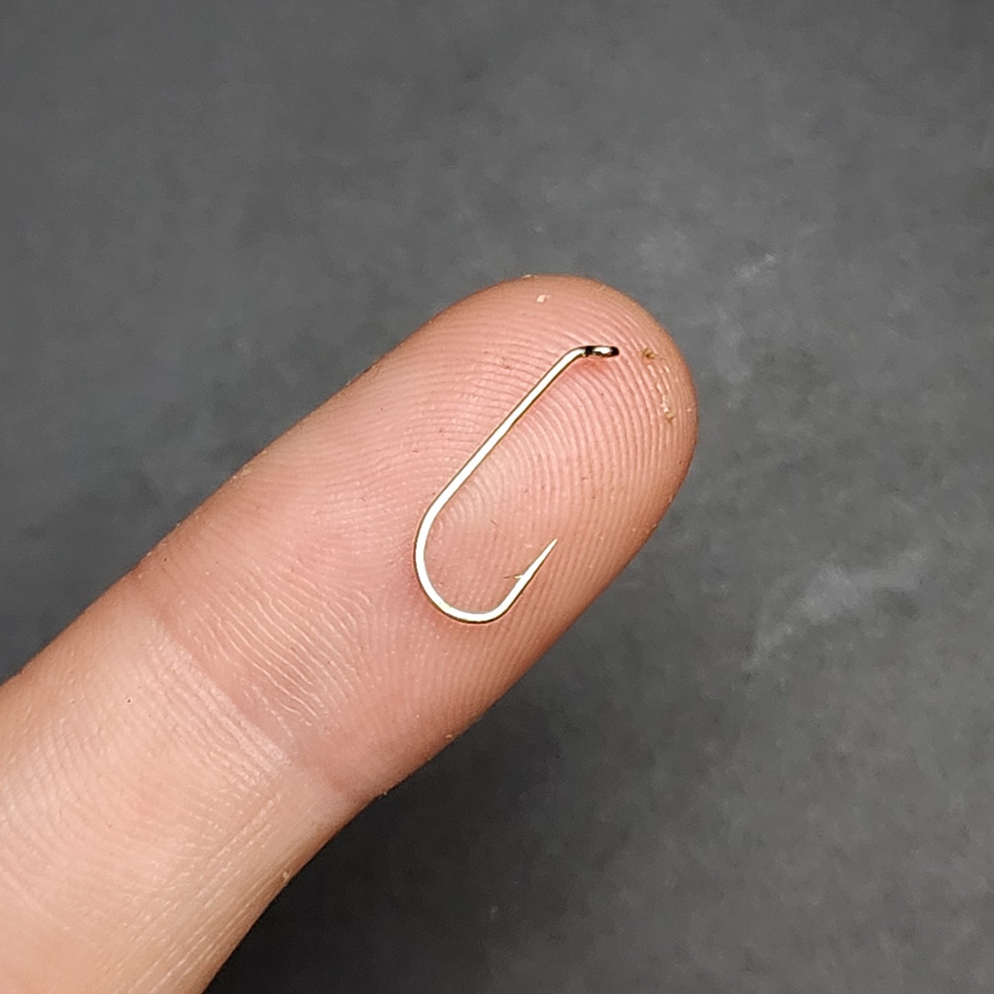 Small silver fishing hook on a finger against a dark background