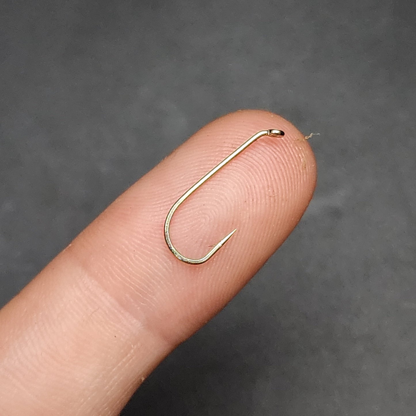 Gold fishing hook held between fingers against a dark background