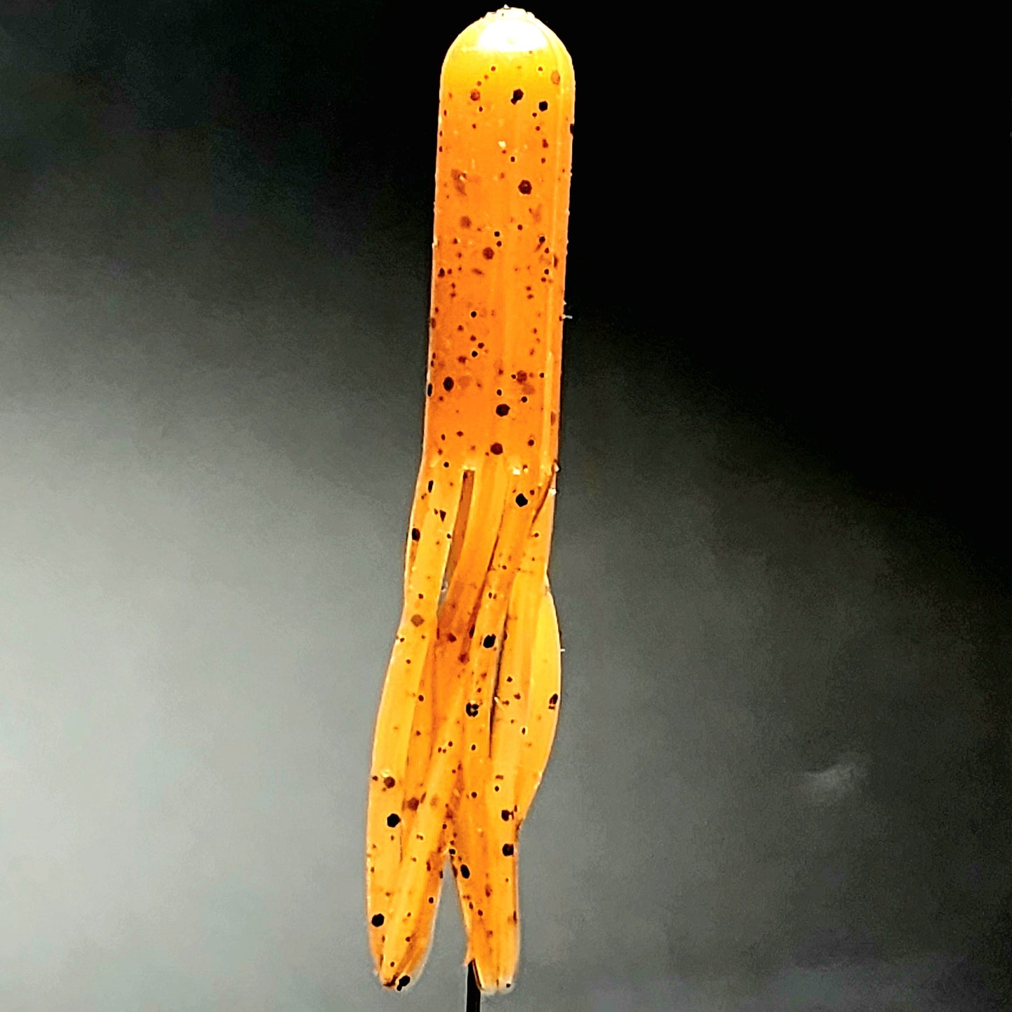 Long, thin, Whisker-Doodle Dangleworm Fishing Lure with black spots on a dark background