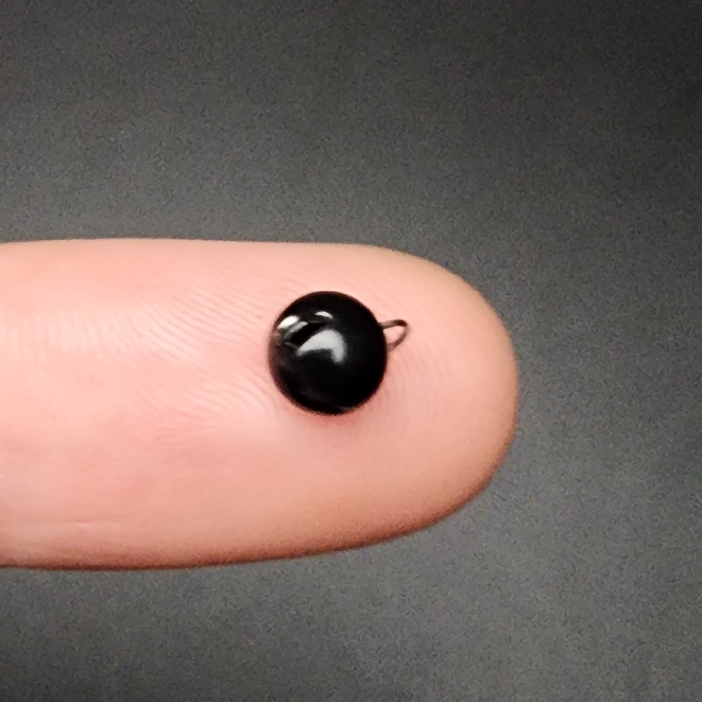 Small black fishing sinker on a finger against a dark background