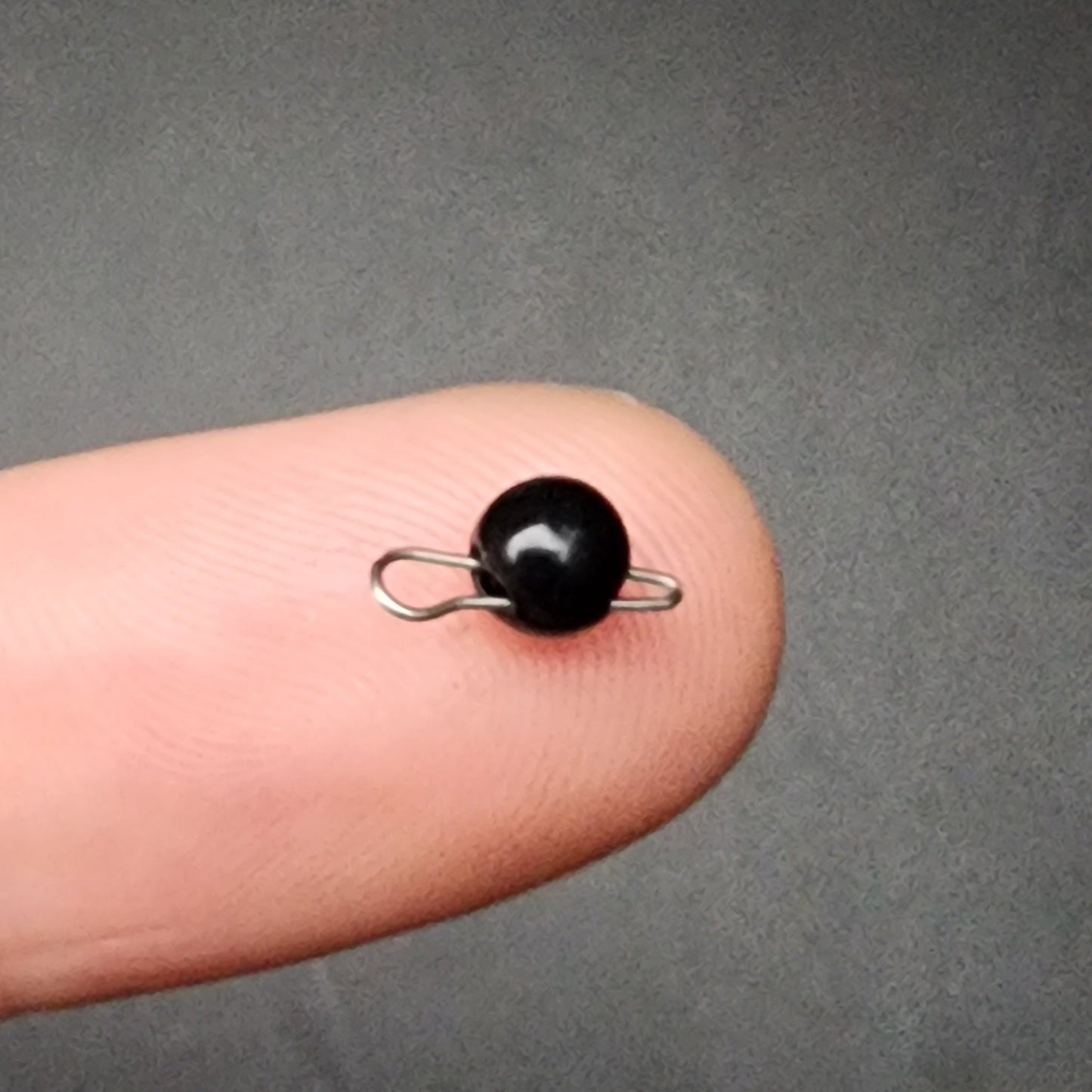 Small black bead sinker with a silver loop on a finger against a gray background