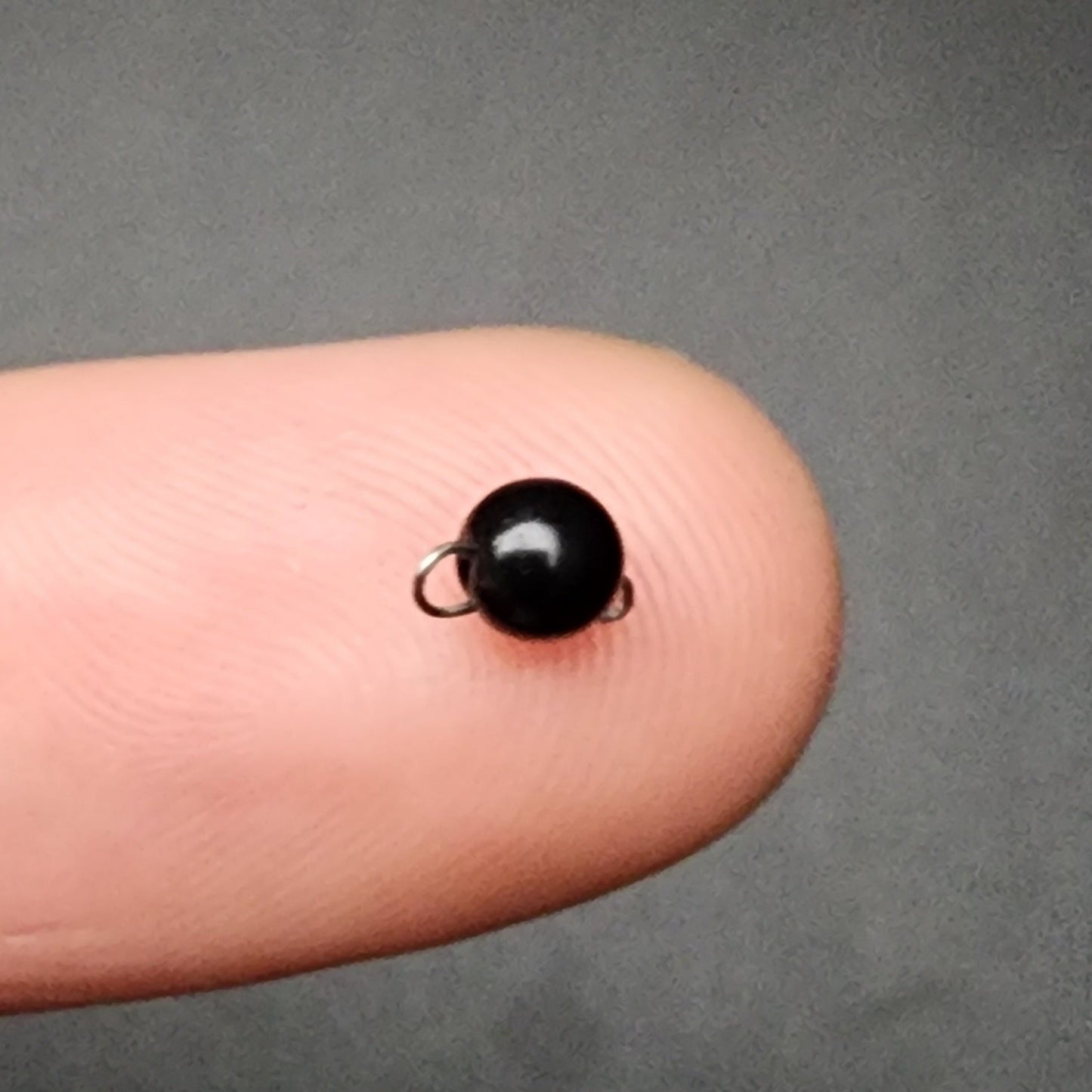 Small black bead sinker on a finger against a gray background