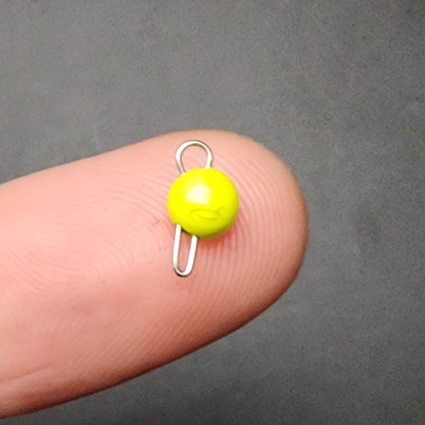 Small yellow sinker on a finger against a gray background