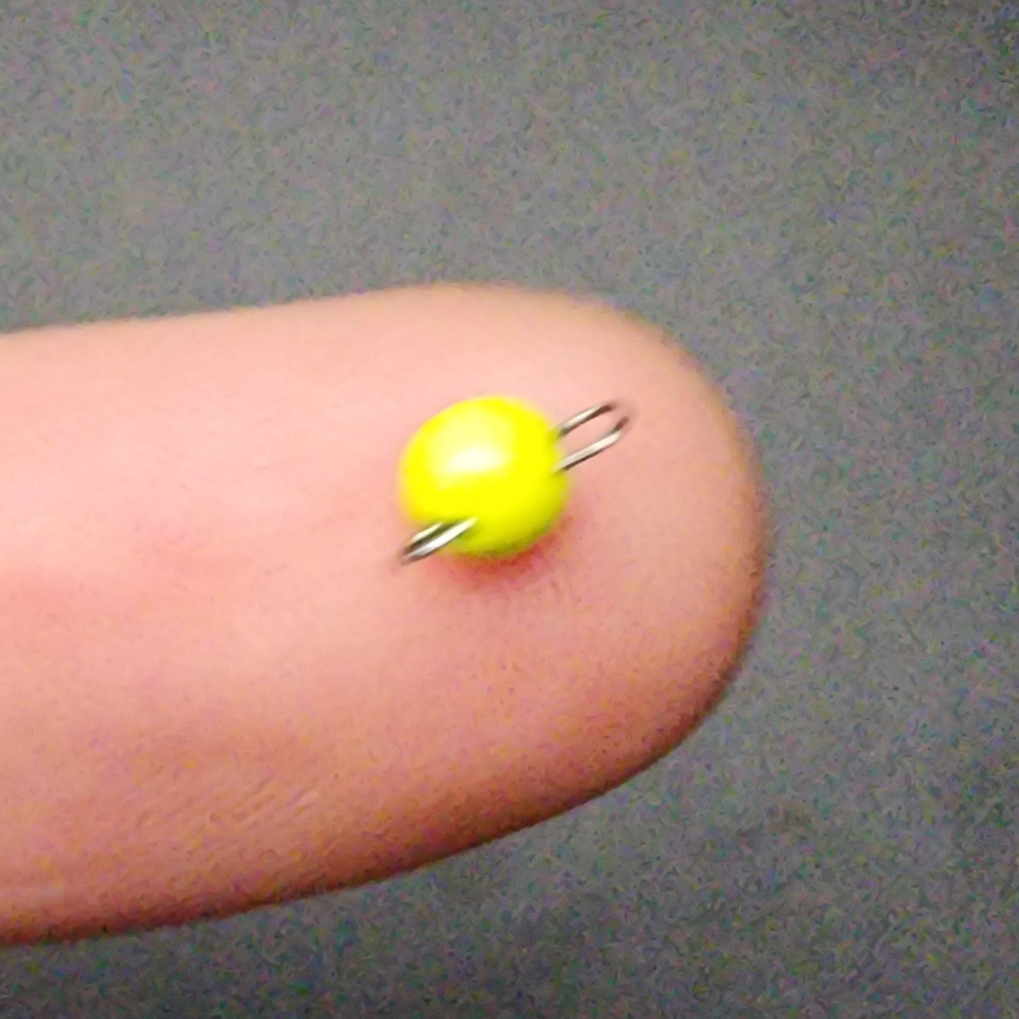 Yellow sinker held between fingers against a gray background