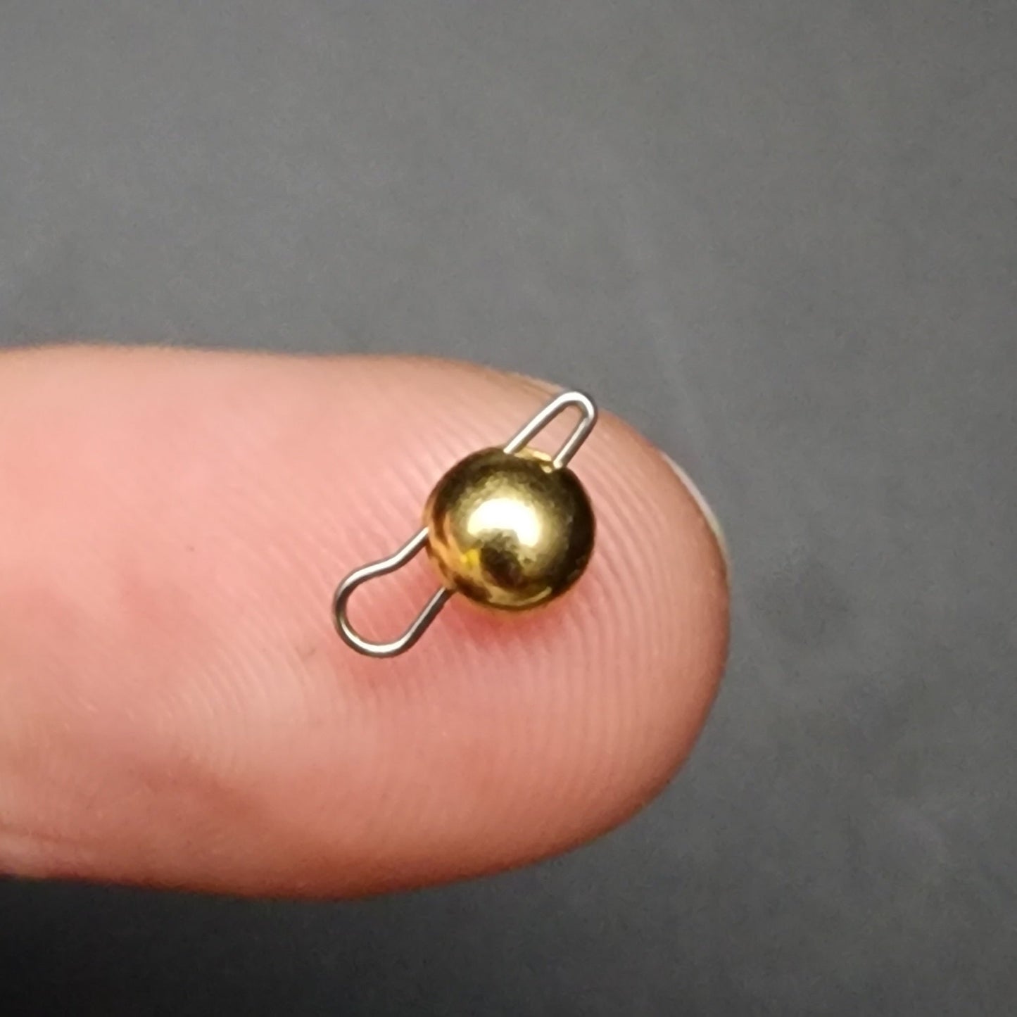 Small gold and silver sinker and clip on a finger against a gray background