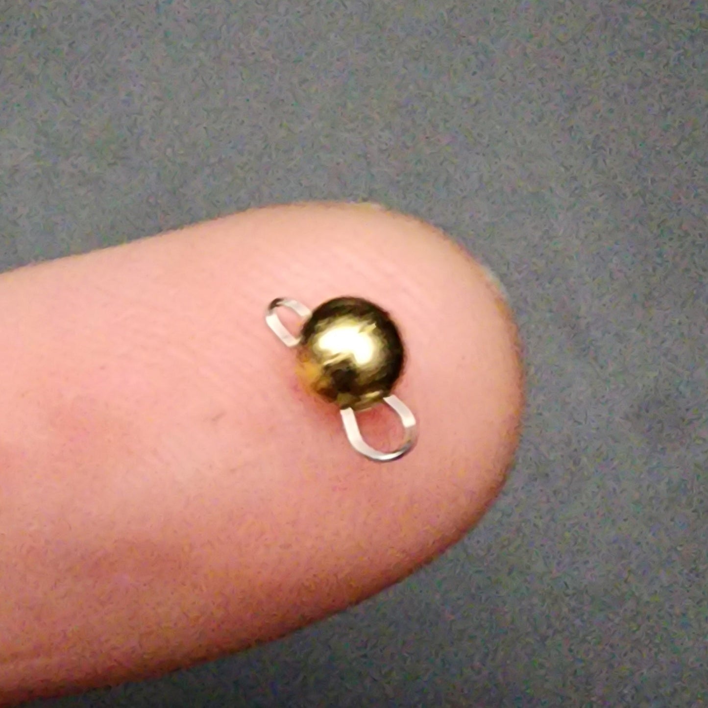 Small gold and silver sinker on a finger against a gray background
