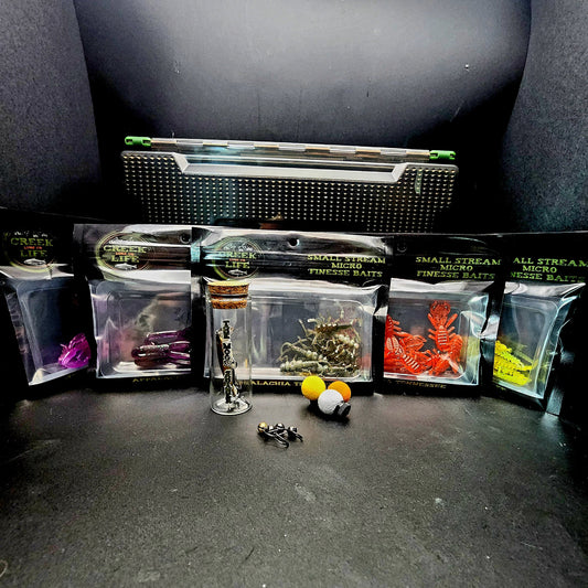 Collection of small fishing lures and baits on a dark surface with a black background.