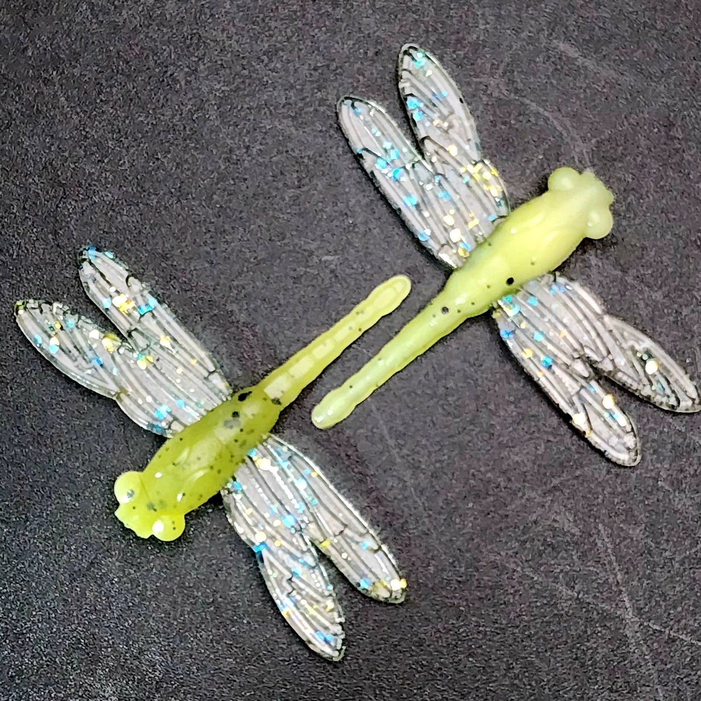 Two dragonfly-shaped fishing lures on a dark surface