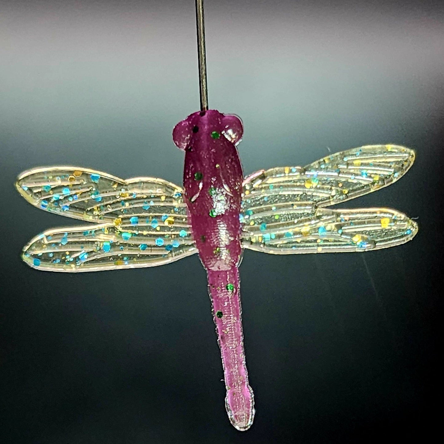 Dragonfly fishing lure with pink body and transparent wings on a dark background