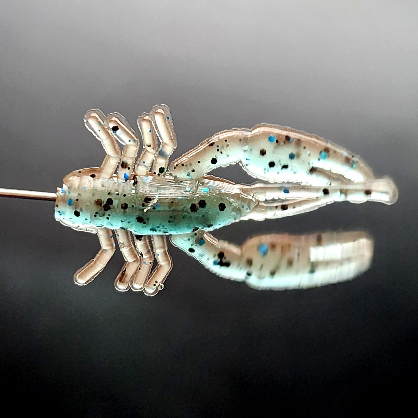 Crawfish shaped fishing lure with a reflective surface on a dark background