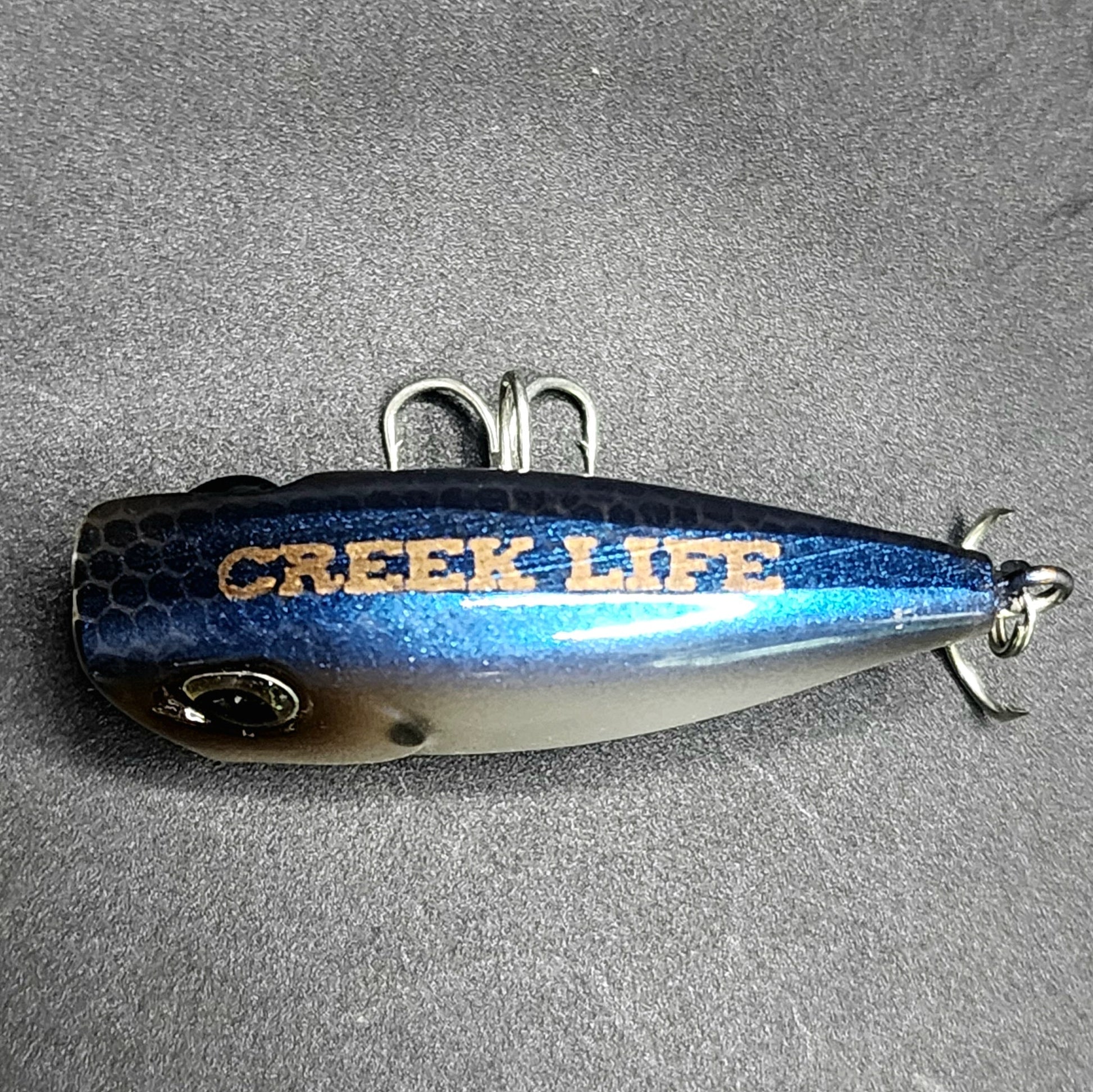Fishing lure with 'Creek Life' branding on a gray background