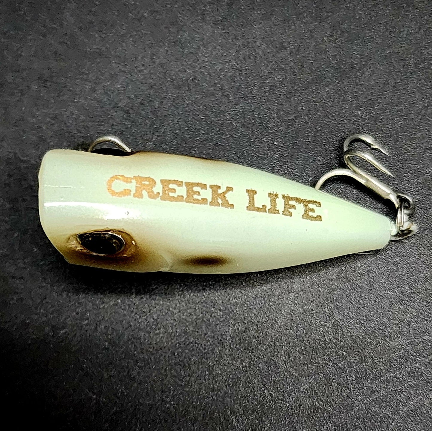 Fishing lure with 'Greek Life' branding on a dark background