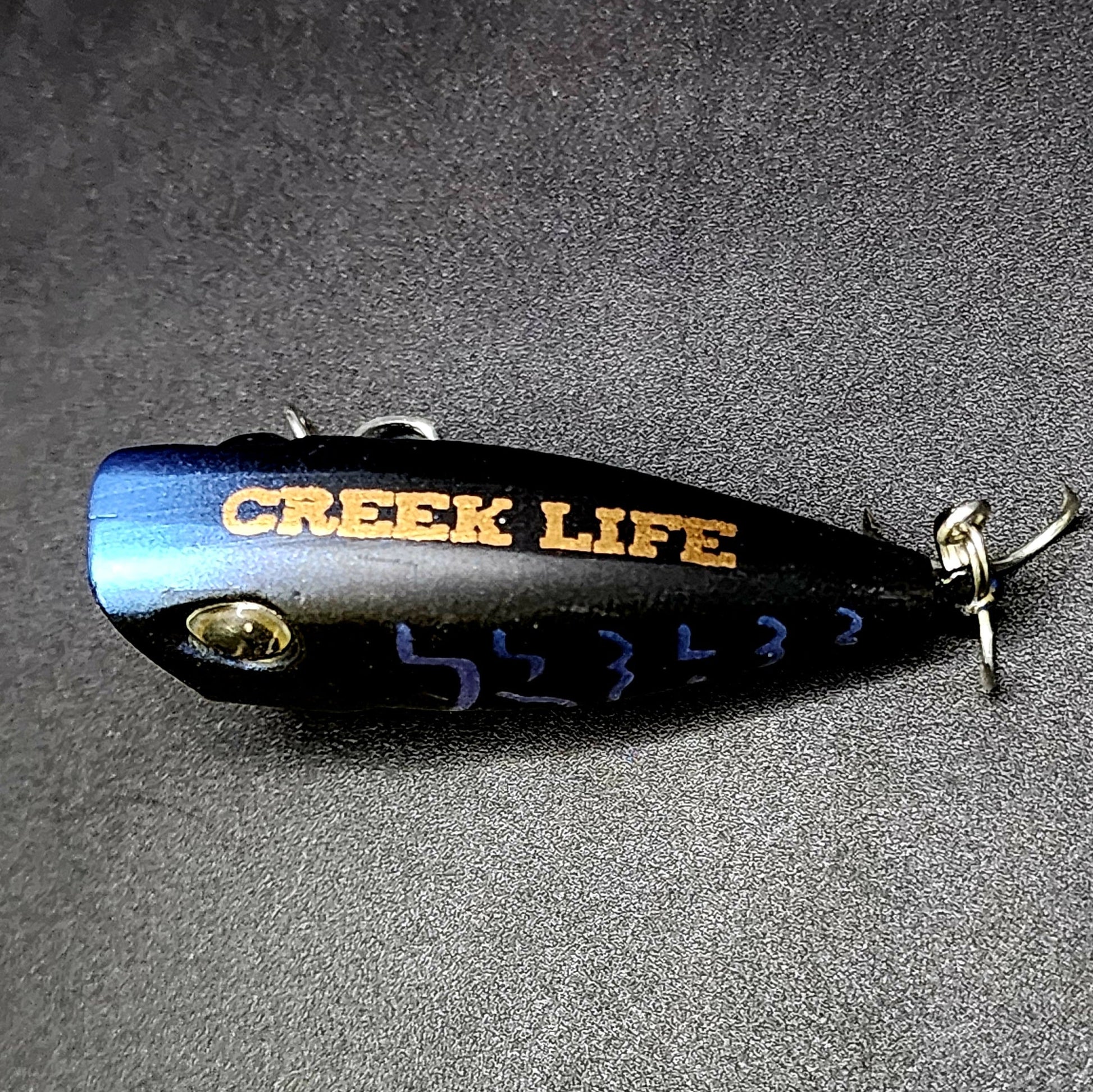 Fishing lure with 'Creek Life' branding on a gray background