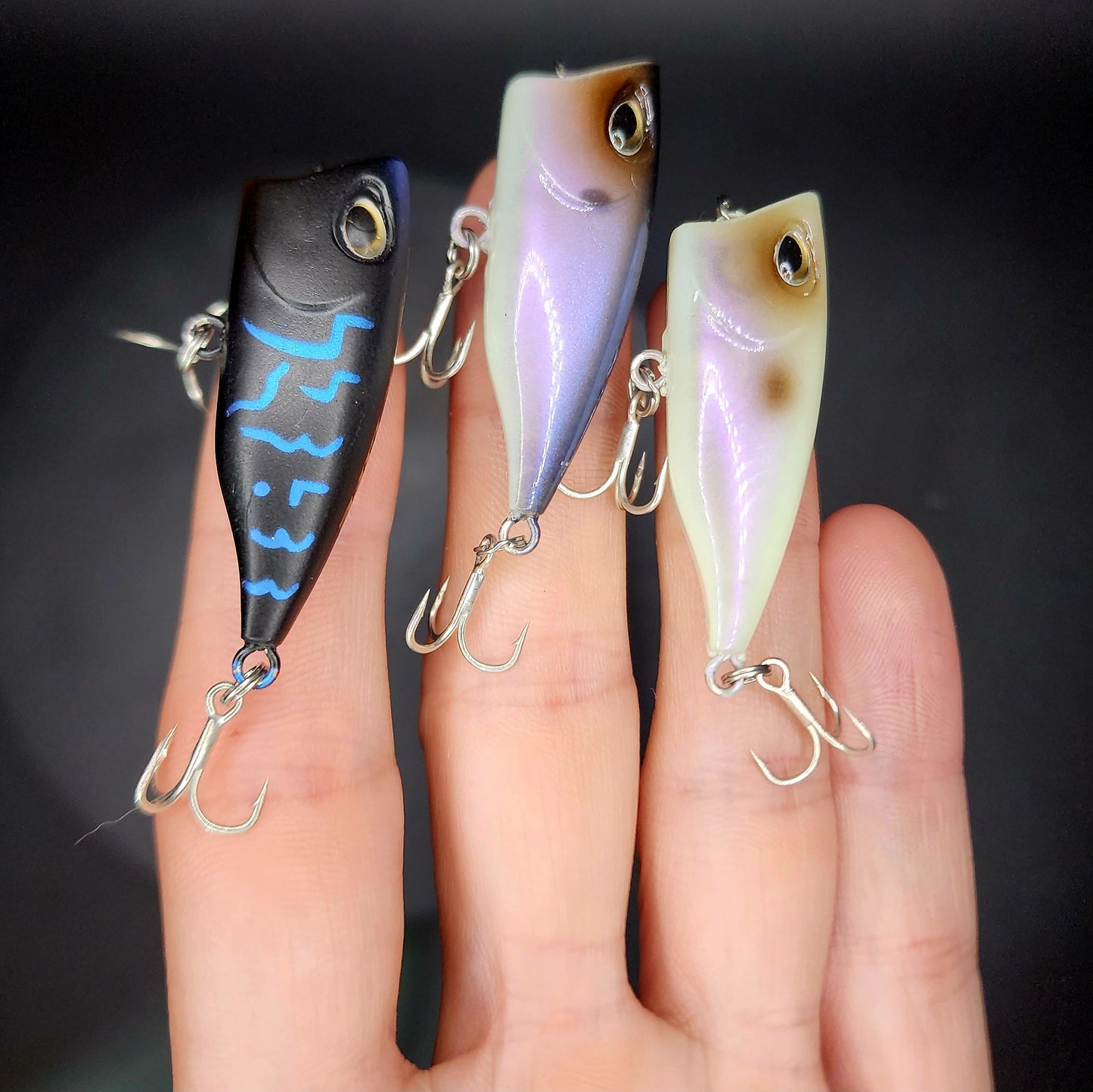 Three fishing lures held in a hand against a dark background