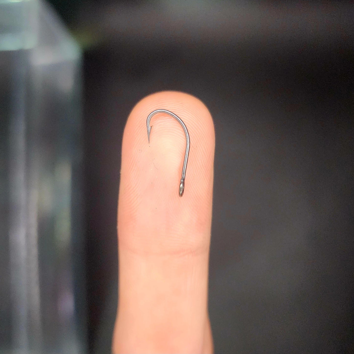 Fishing hook on a finger against a dark background