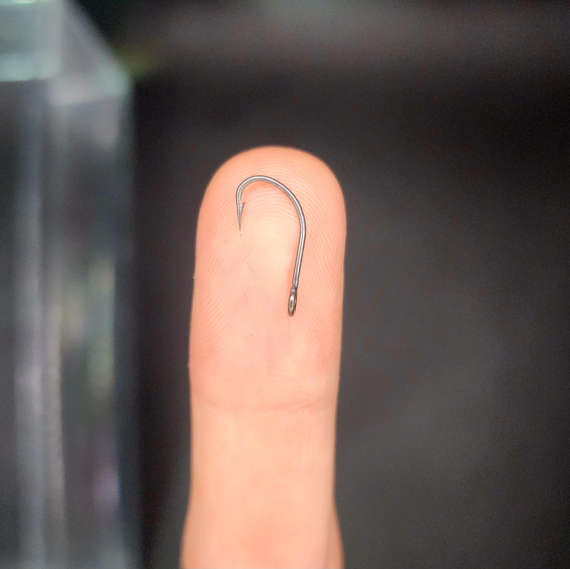 Fishing hook on a finger against a dark background