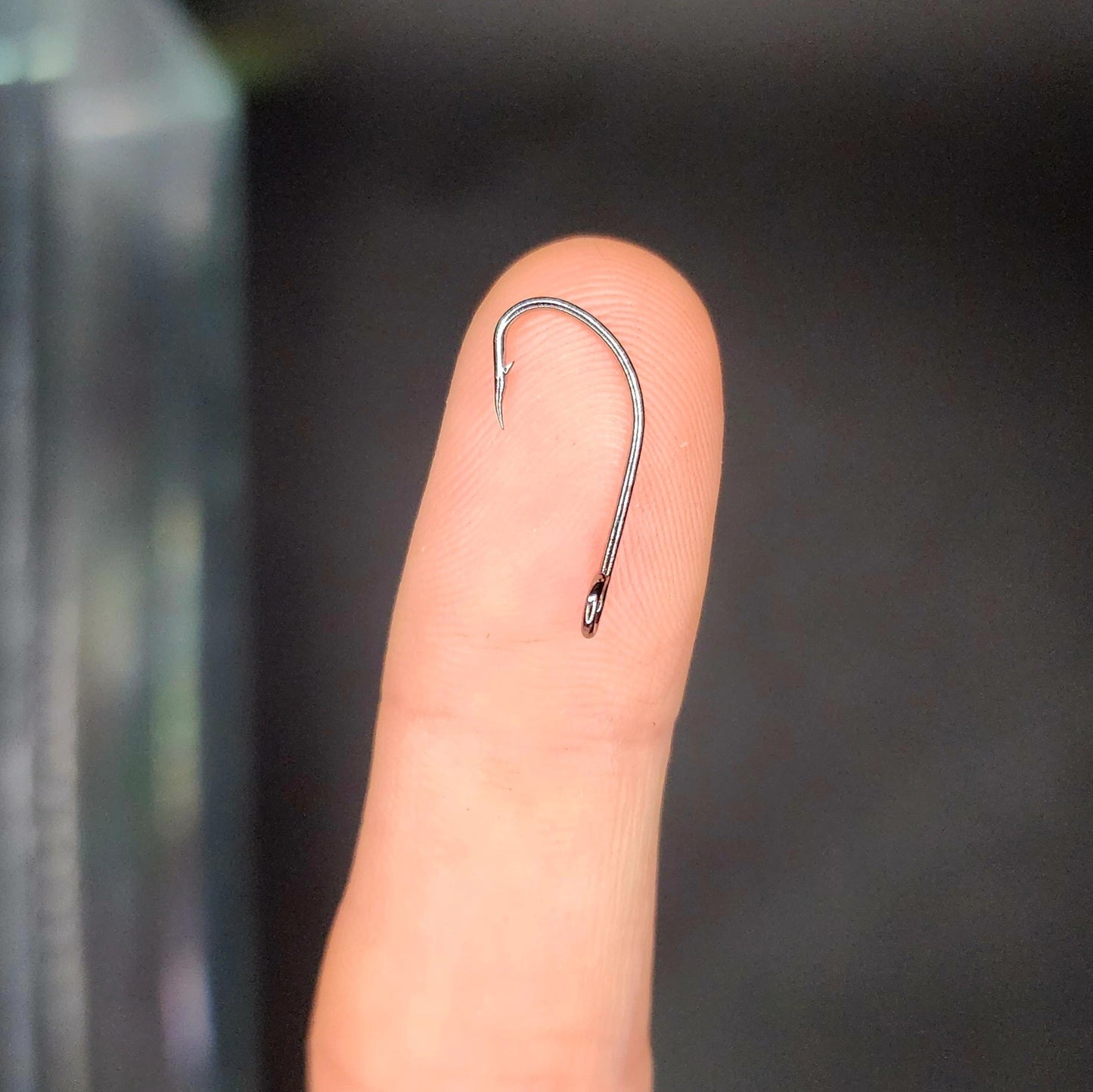 Small fishing hook on a finger against a dark background