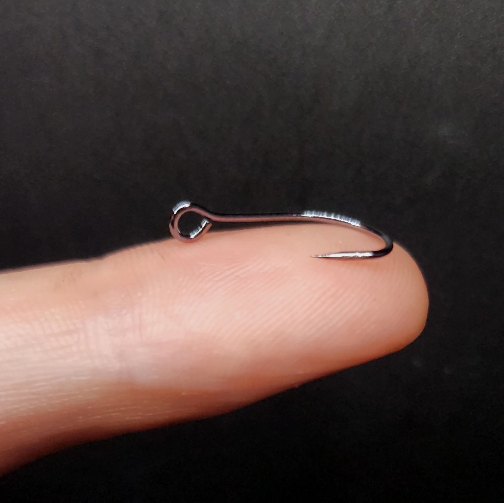 Silver fish hook on a finger against a dark background