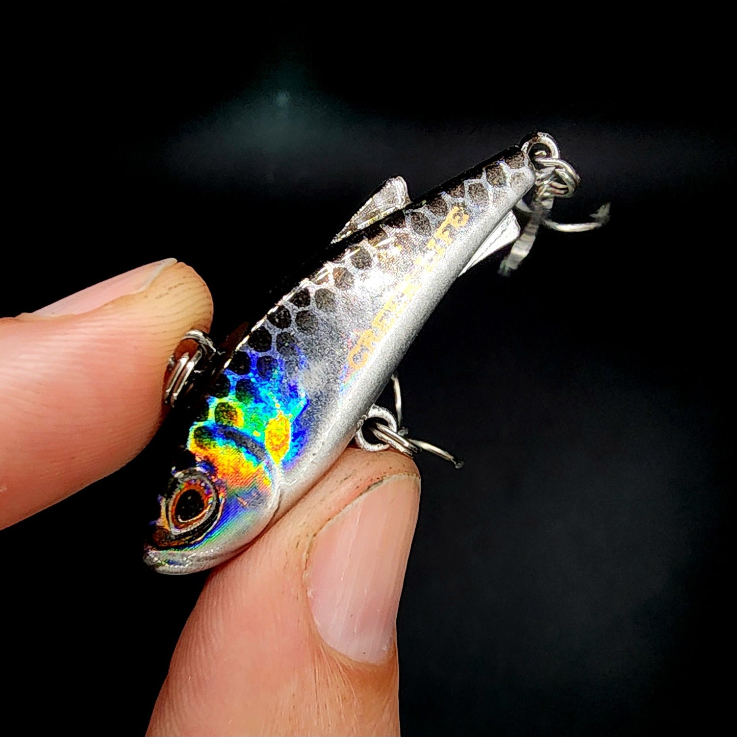 Fishing lure held between fingers against a dark background