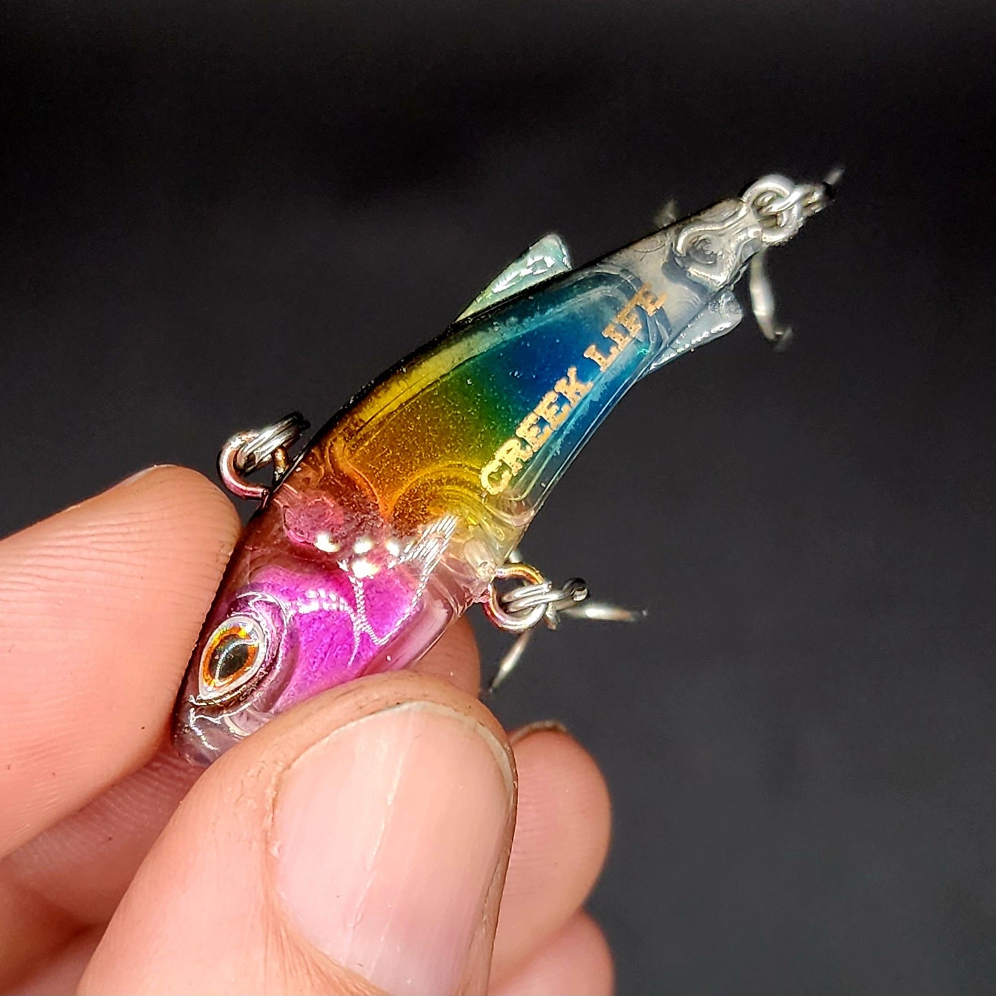 Colorful fishing lure held by a hand against a dark background