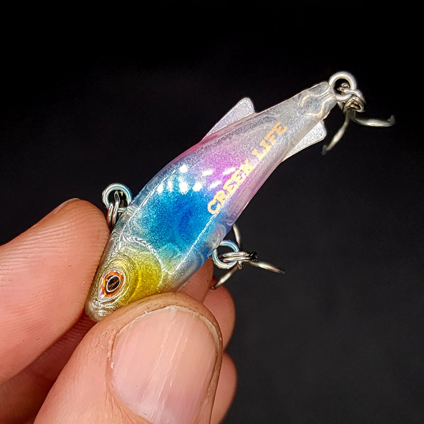 Colorful fishing lure held in a hand against a dark background