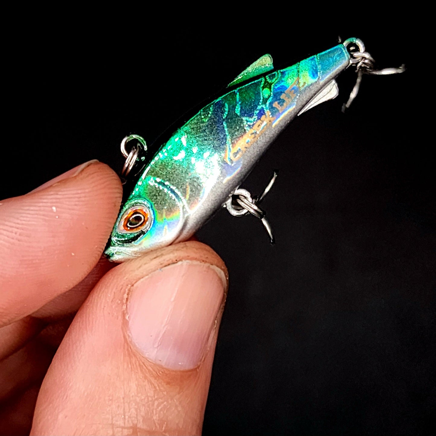 Fishing lure held in a hand against a black background