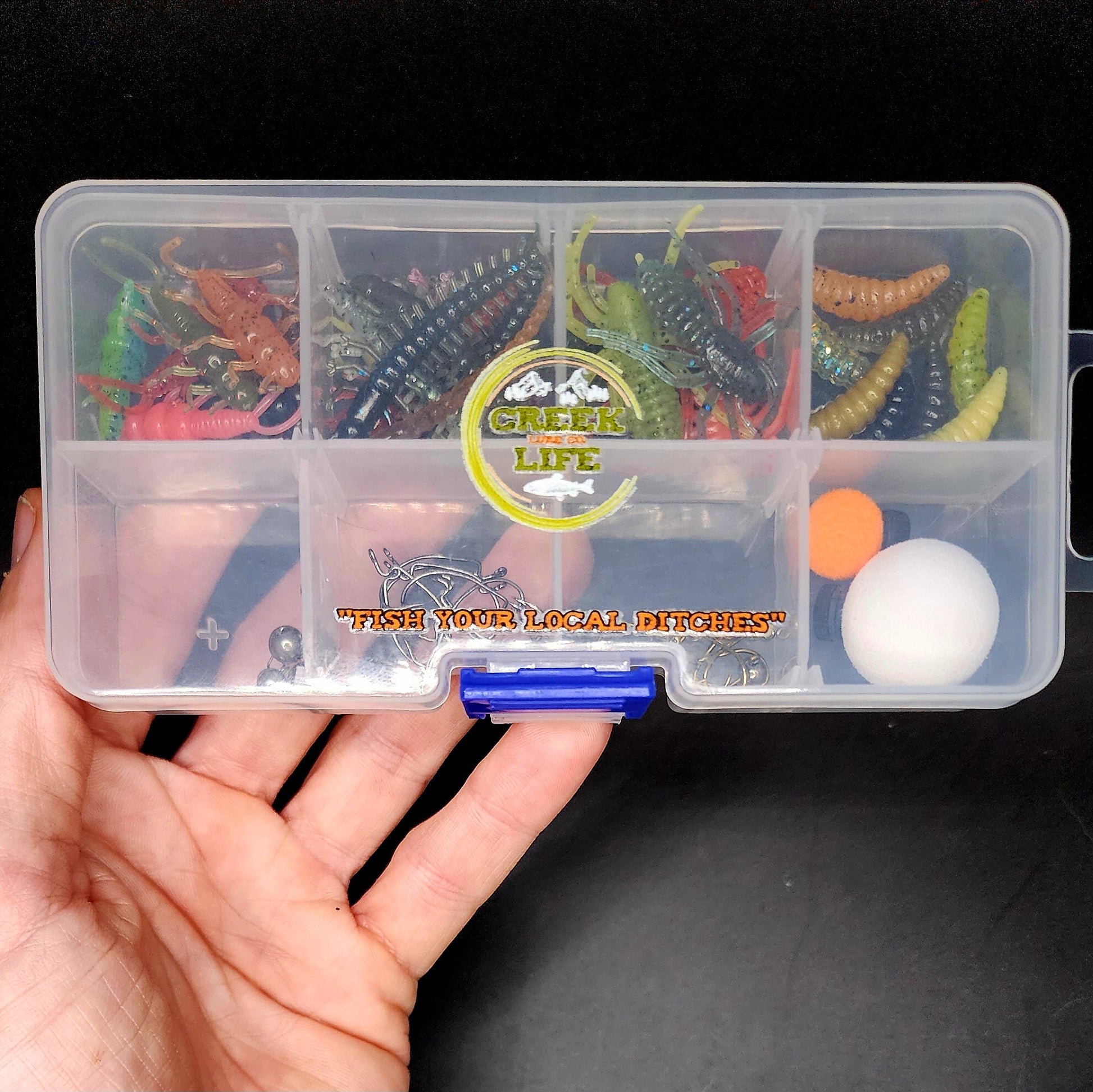 Fishing lure box with various lures held by a hand on a black background