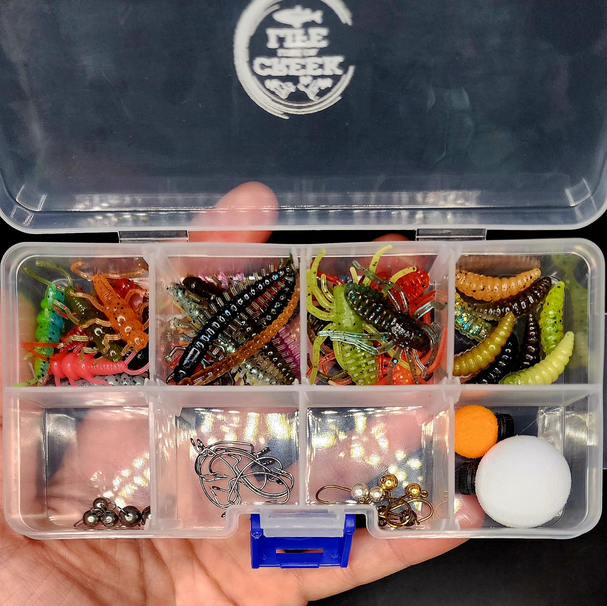 Fishing lure set in a tackle box held by a hand, with a visible brand logo on the lid.