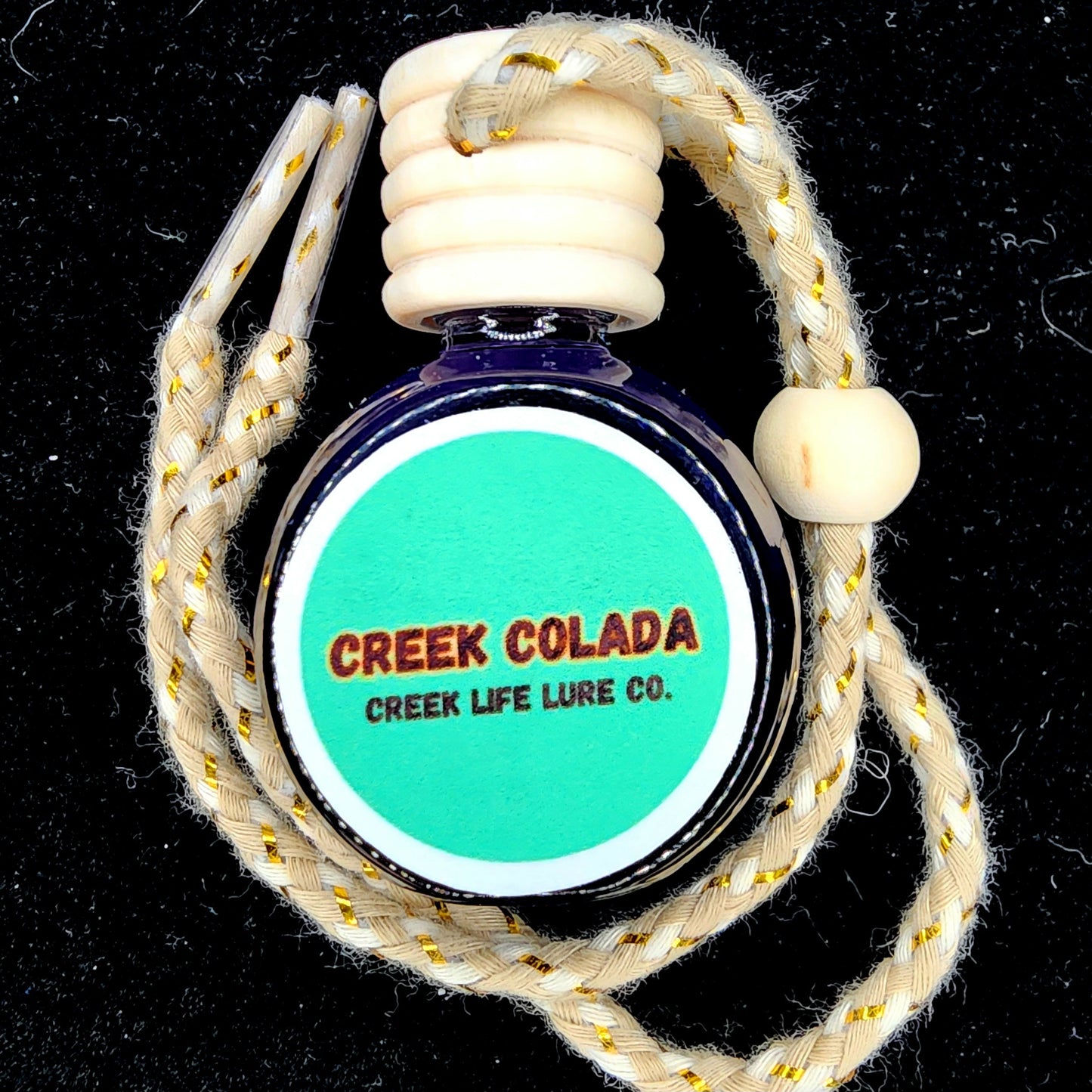 Bottle of 'Creek Colada' by Creek Life Lure Co. with braided rope on a black background