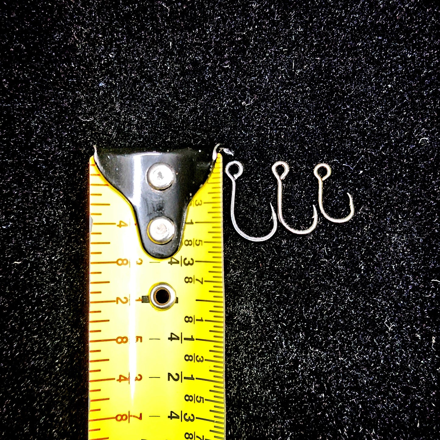Three fishing hooks next to a measuring tape on a black background