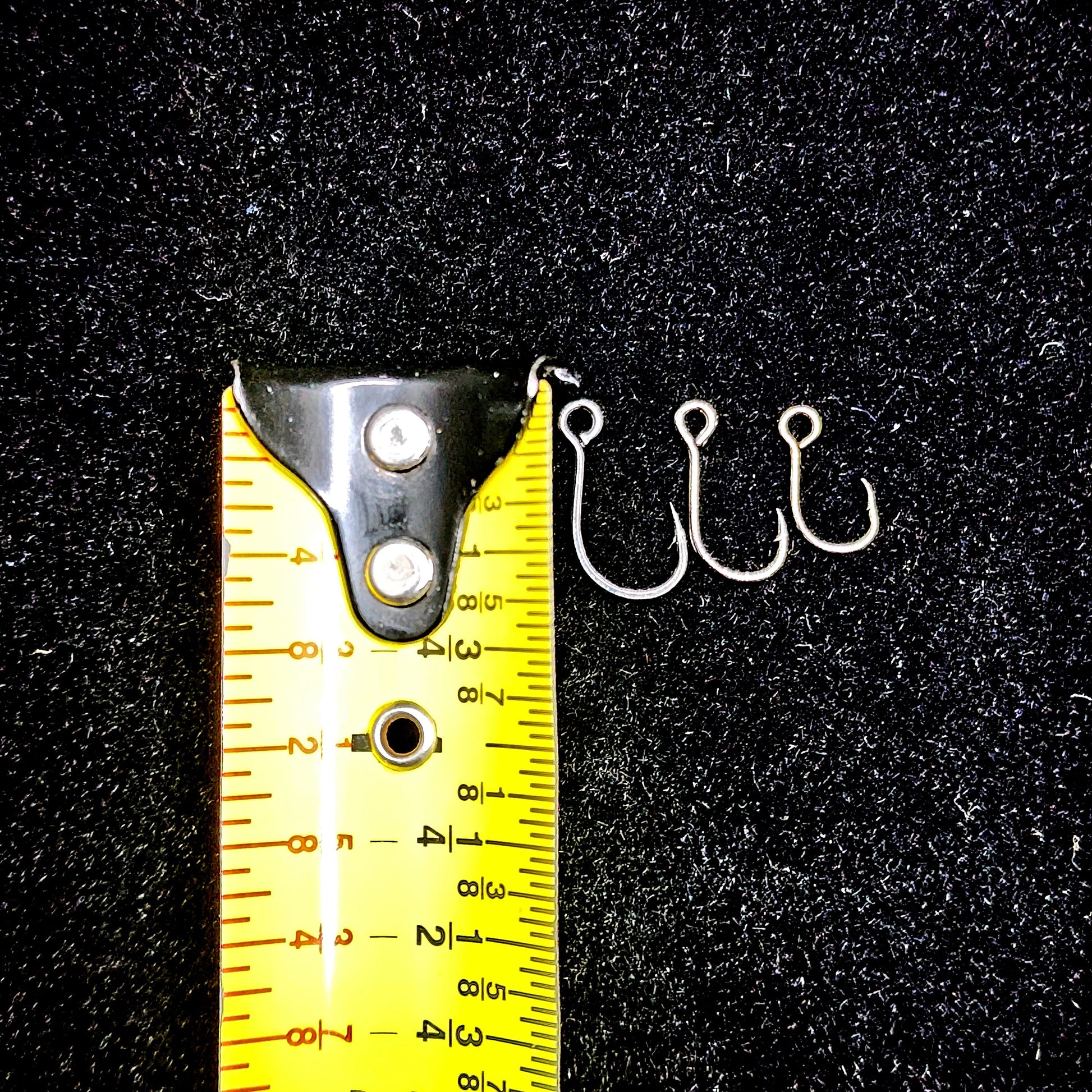 Three fishing hooks next to a measuring tape on a black background