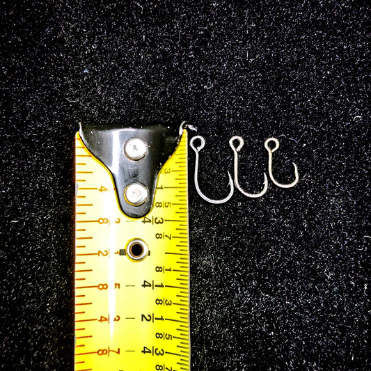 Three fishing hooks next to a measuring tape on a black background