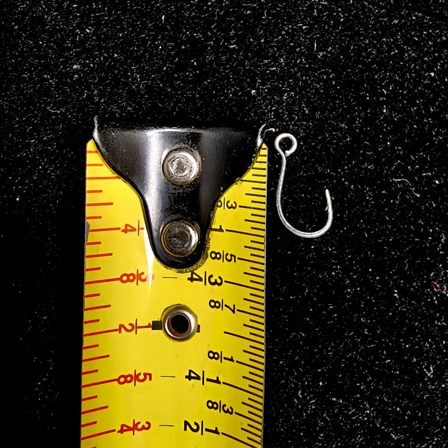 Fishing hook with a measuring tape for scale on a black background